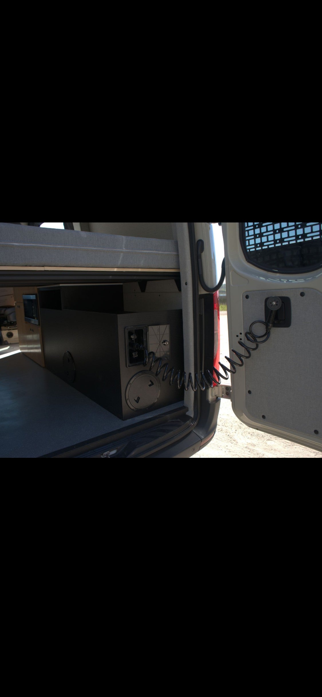 RV rental's rear utility area with under-bed storage, control panel, and coiled outdoor shower hose.