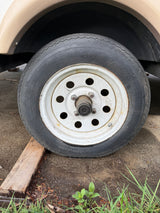 A 4.80-12 trailer tire, marked 'FOR TRAILER USE ONLY', on a white wheel, often found with an RV rental, resting on a wooden block.