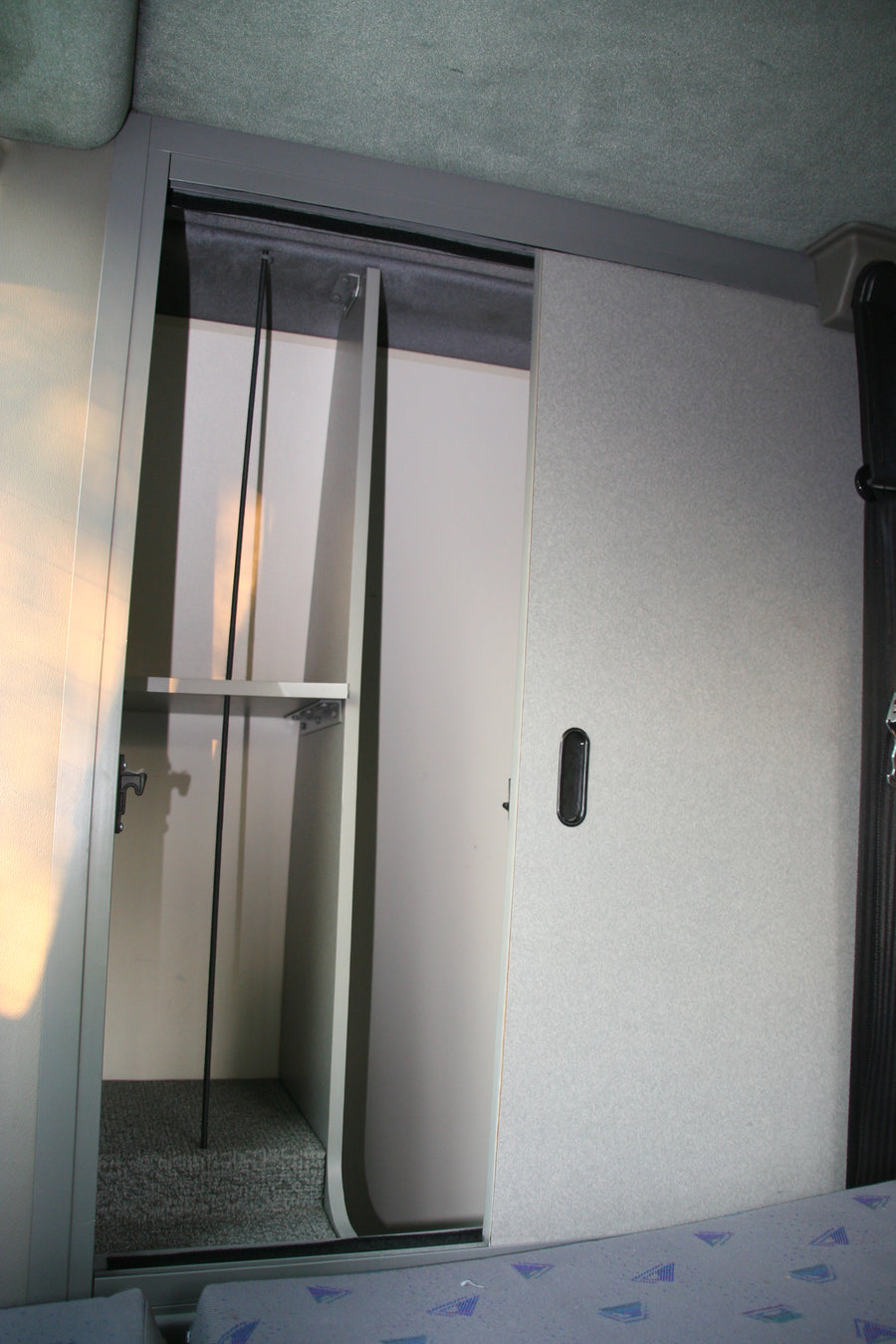Open overhead storage with shelves and a latch in an RV rental interior, showing textured walls and patterned seating.