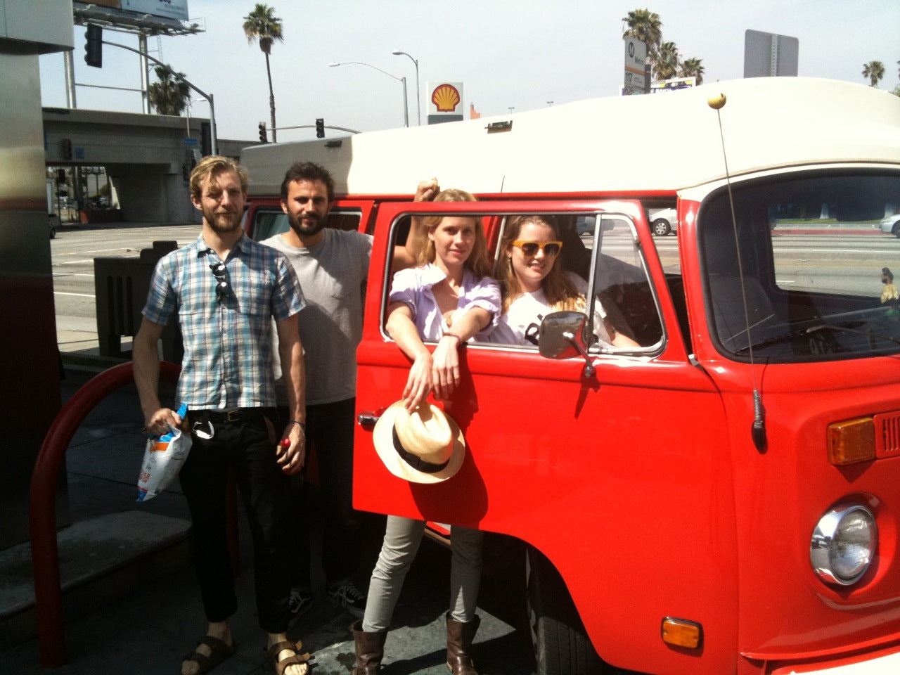 RV rental adventure: Four friends pose with a vibrant red vintage VW van, ready for a sunny road trip.