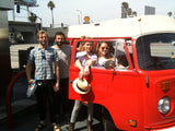 RV rental adventure: Four friends pose with a vibrant red vintage VW van, ready for a sunny road trip.