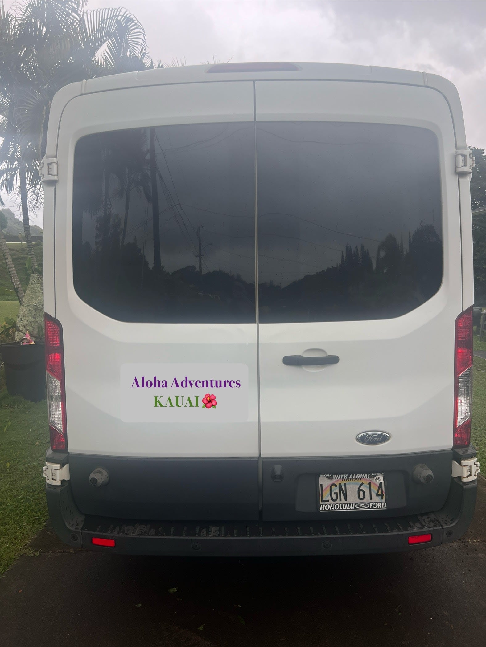 This white Ford van RV rental, with an "Aloha Adventures Kauai" sticker, features Hawaii license plate LGN 614.