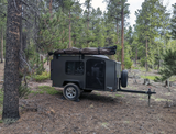 An off-road camper trailer from an RV rental, ready for forest adventures. Perfect for outdoor travel & wilderness camping.