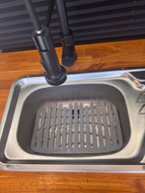 RV rental kitchen sink area: stainless steel sink with mat, black faucet, wood counter, and pleated blinds.