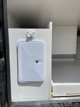 RV rental: White external shower port and spigot on a cabinet, with open storage in this camper van interior.
