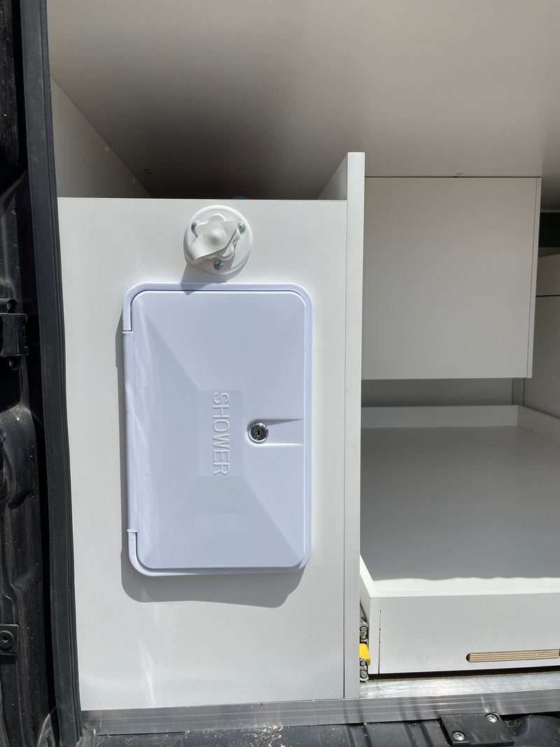 RV rental: White external shower port and spigot on a cabinet, with open storage in this camper van interior. — photo 17