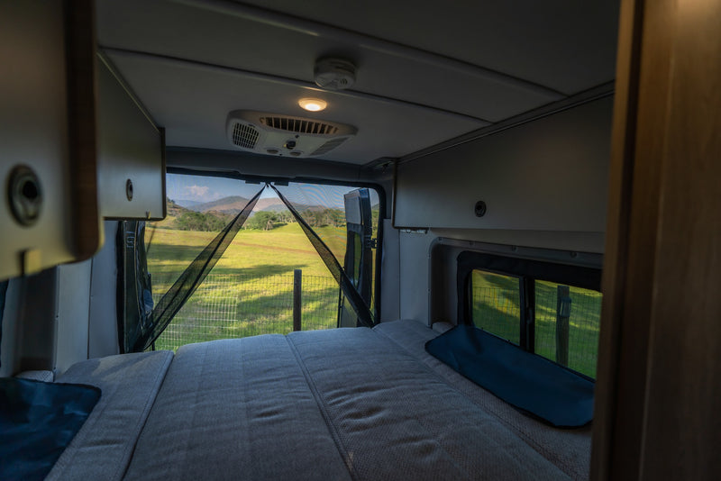 Relax inside this cozy RV rental, featuring a comfortable bed and a stunning view of green fields and mountains through the mosquito-netted rear doors. — photo 13