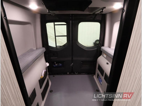 Spacious RV rental interior viewed from front, showing twin sleeping benches, rear doors, and organized storage for camper adventures.
