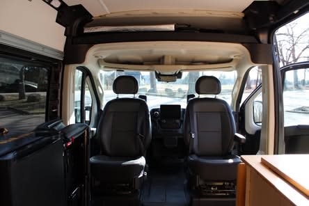 RV rental: Inside view of the front cabin with black driver & passenger seats, dashboard, and open side door.