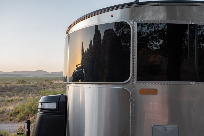 Close-up of a silver Airstream rv rental, its front windows reflecting jagged desert peaks at sunset. — photo 5