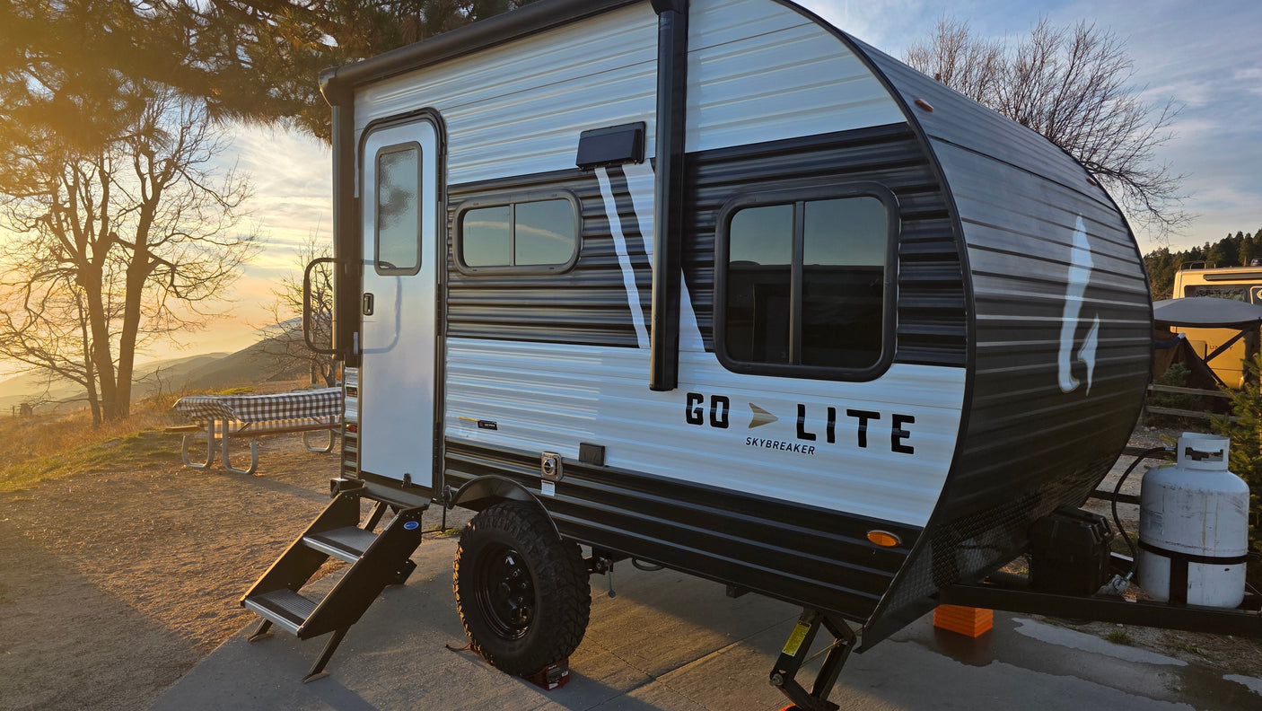 A white & black Go Lite Skybreaker RV rental travel trailer parked in a scenic mountain campsite during sunset.