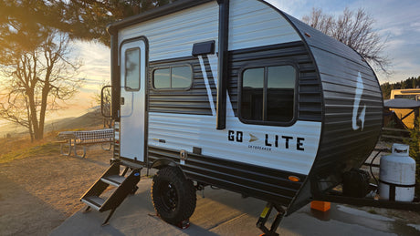 A white & black Go Lite Skybreaker RV rental travel trailer parked in a scenic mountain campsite during sunset.