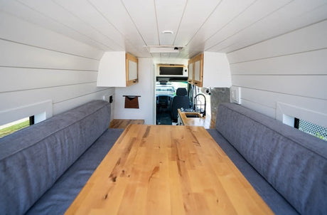 Modern RV rental interior: bright camper van dining area with wooden table, cozy benches, and compact kitchen setup.