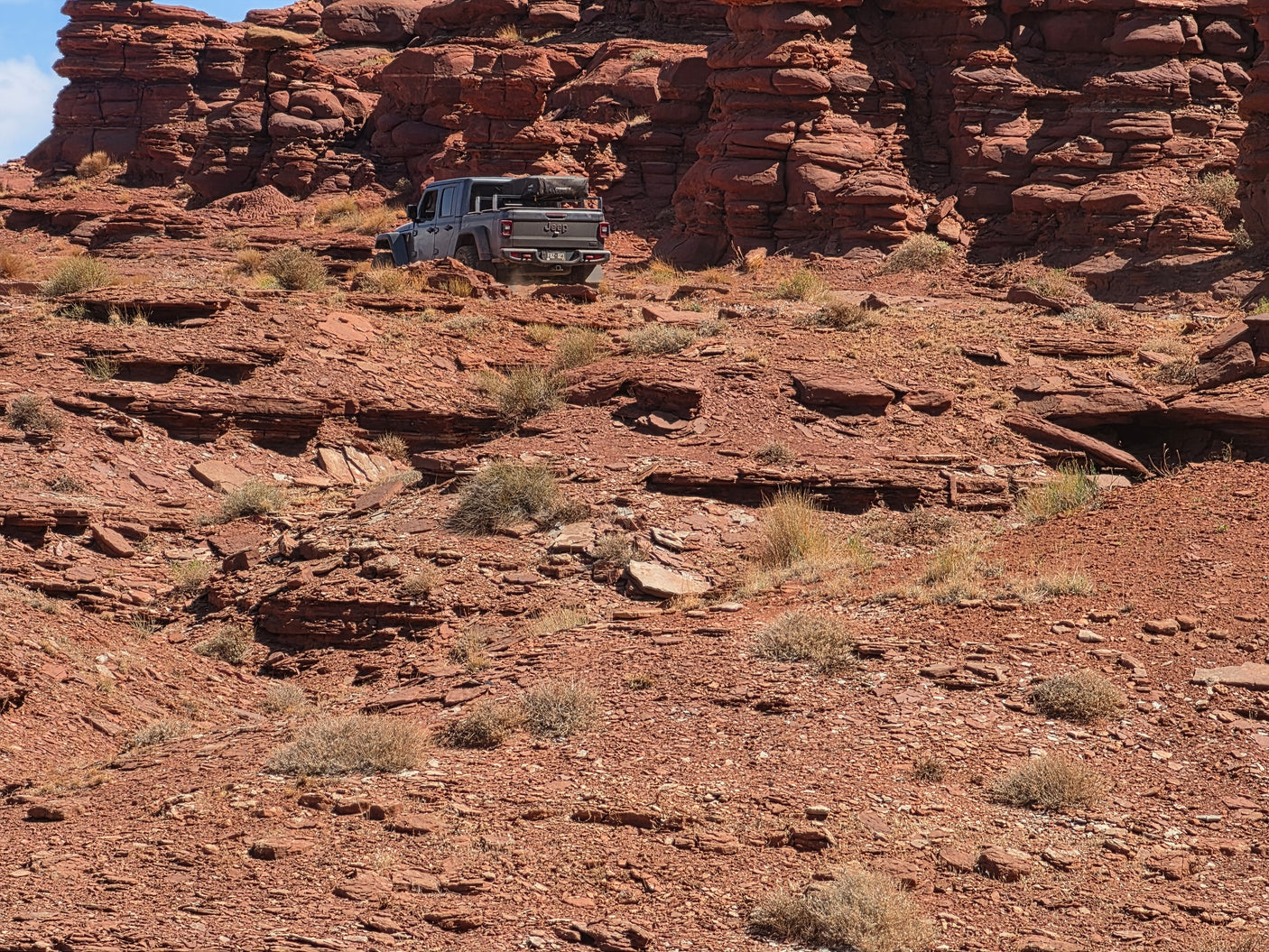 A grey Jeep Gladiator with rooftop tent on a rugged, rocky red desert trail. Explore off-road adventure, an rv rental opens possibilities.