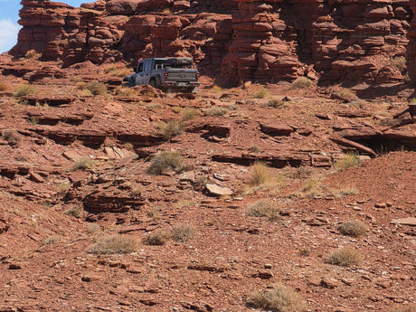 A grey Jeep Gladiator with rooftop tent on a rugged, rocky red desert trail. Explore off-road adventure, an rv rental opens possibilities.