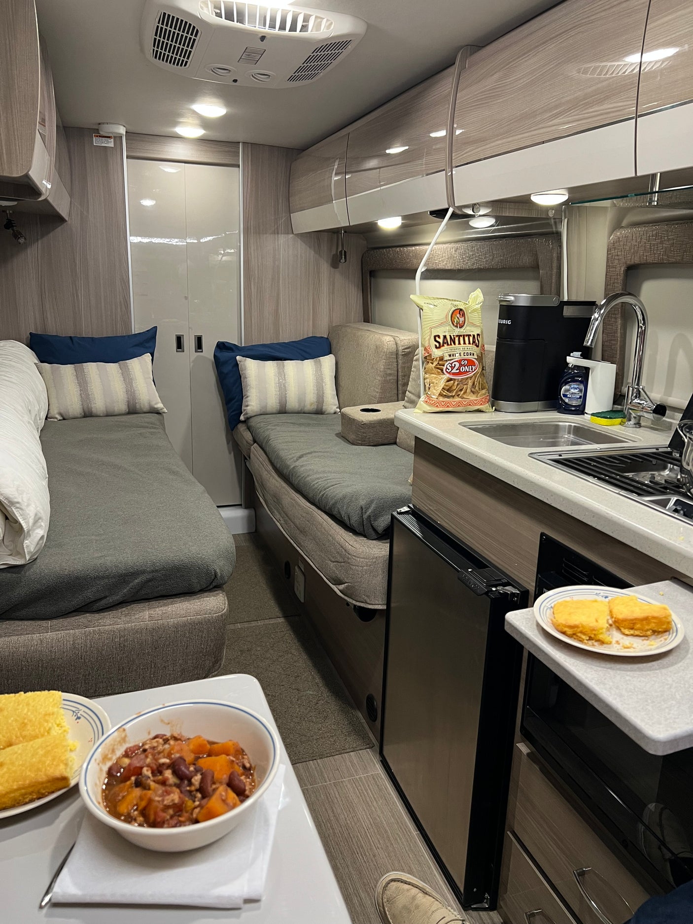 Inside a cozy RV rental: two sleeping/lounge areas, a kitchenette with coffee and snacks, plus a warm meal ready.