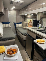 Inside a cozy RV rental: two sleeping/lounge areas, a kitchenette with coffee and snacks, plus a warm meal ready.