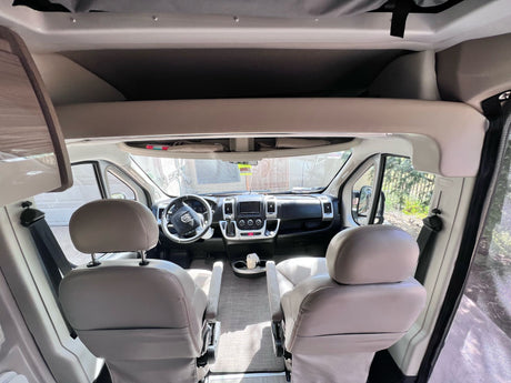 Swivel seats, dashboard, and overhead bunk visible inside a bright RV rental's front cabin.