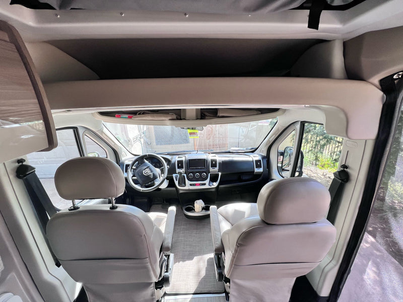 Swivel seats, dashboard, and overhead bunk visible inside a bright RV rental's front cabin. — photo 13