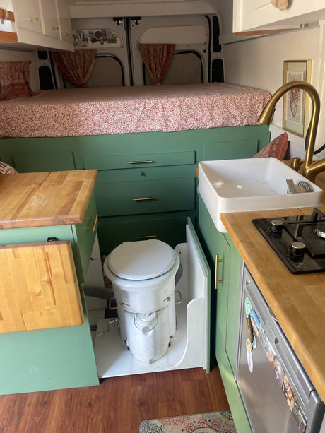 Inside this RV rental: a stylish van conversion with a raised bed, green kitchen cabinets, sink, stove, and pull-out toilet.