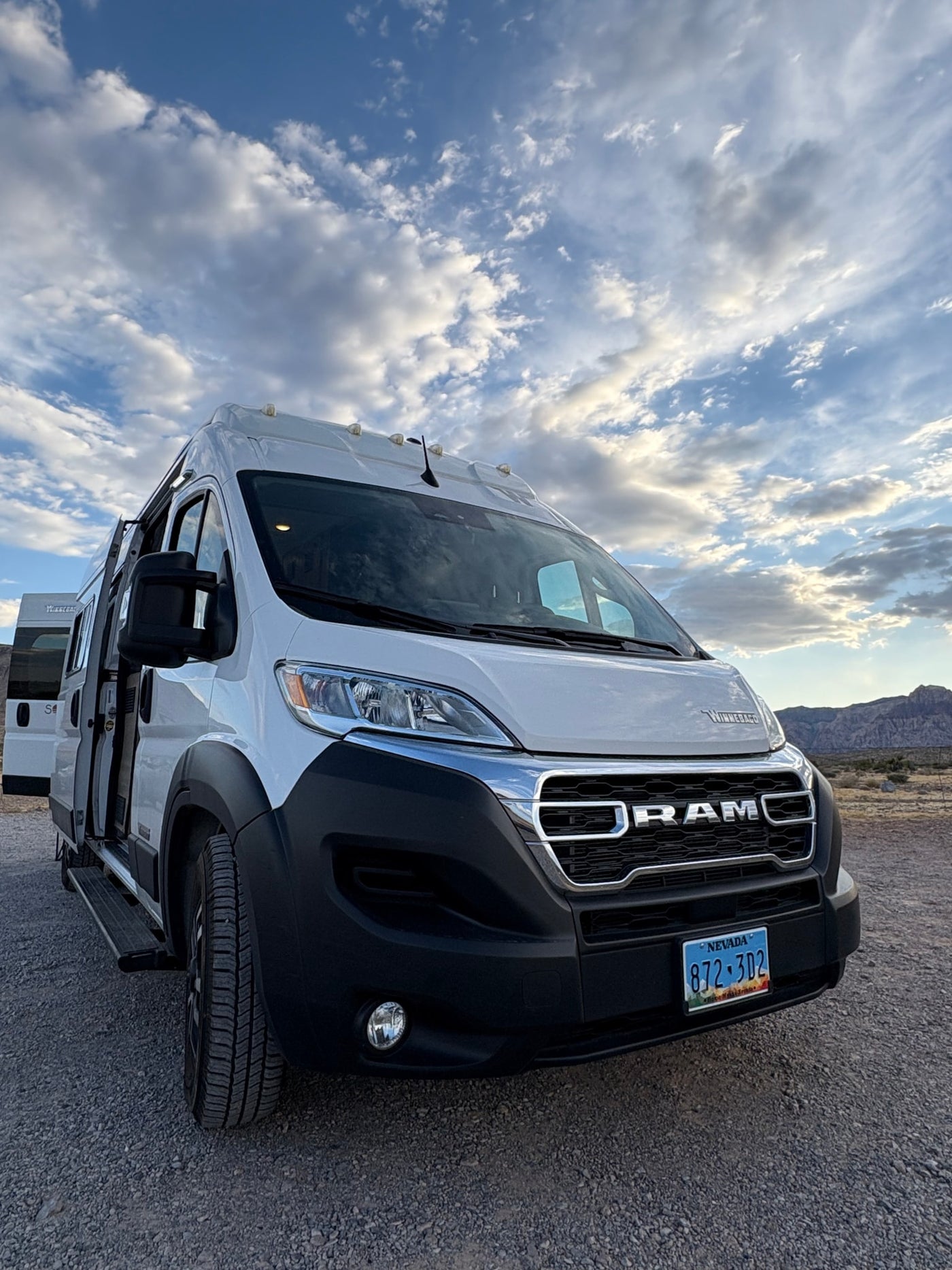 A white Ram RV rental van, parked on a gravel lot under a dramatic cloudy sky, with mountains in the background. — photo 5