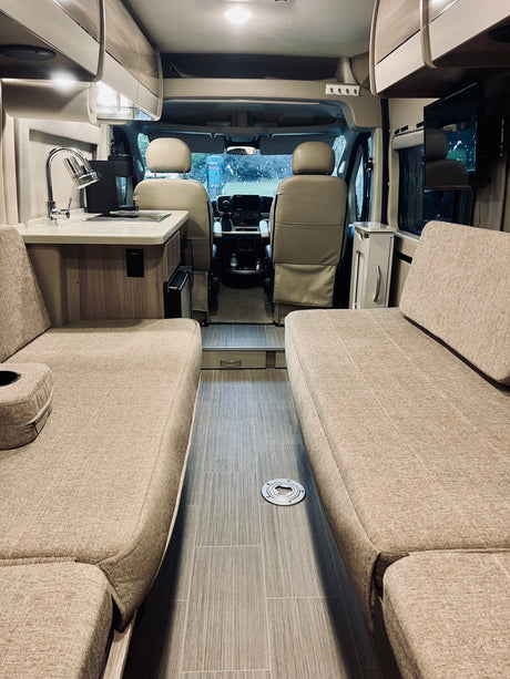 Interior view of a modern rv rental, featuring comfortable benches, a compact kitchen, and the cockpit area.