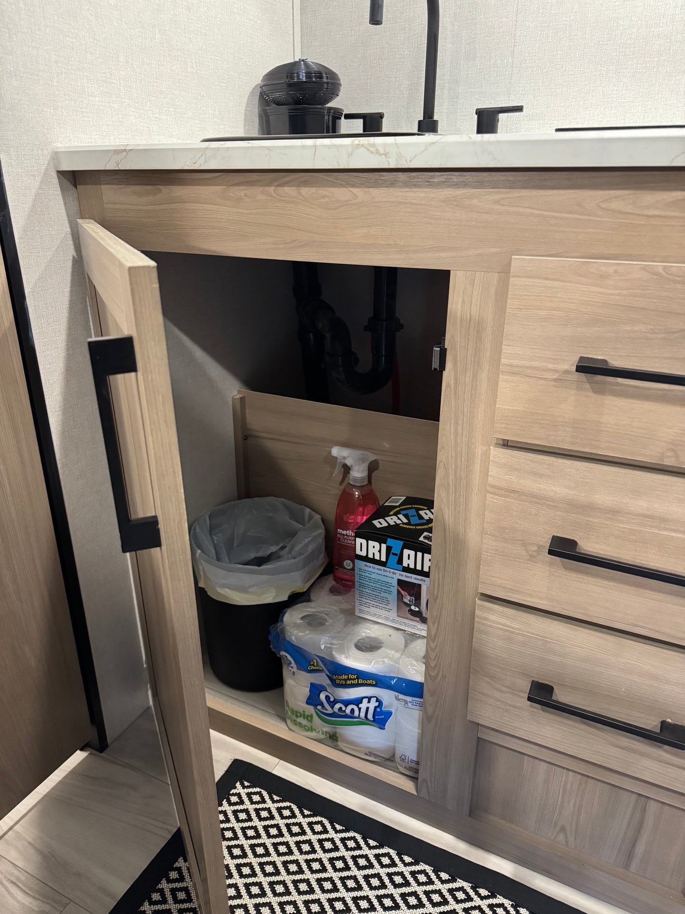 Organized RV rental bathroom vanity storage with specialized toilet paper, cleaner, and a moisture absorber.
