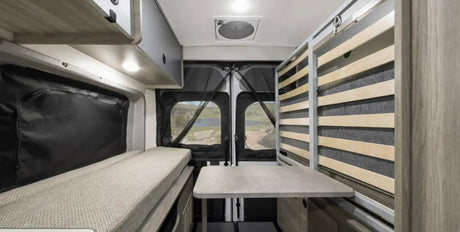 This RV rental interior features a convertible bed, dining table, and screened rear doors showcasing a beautiful lake view.