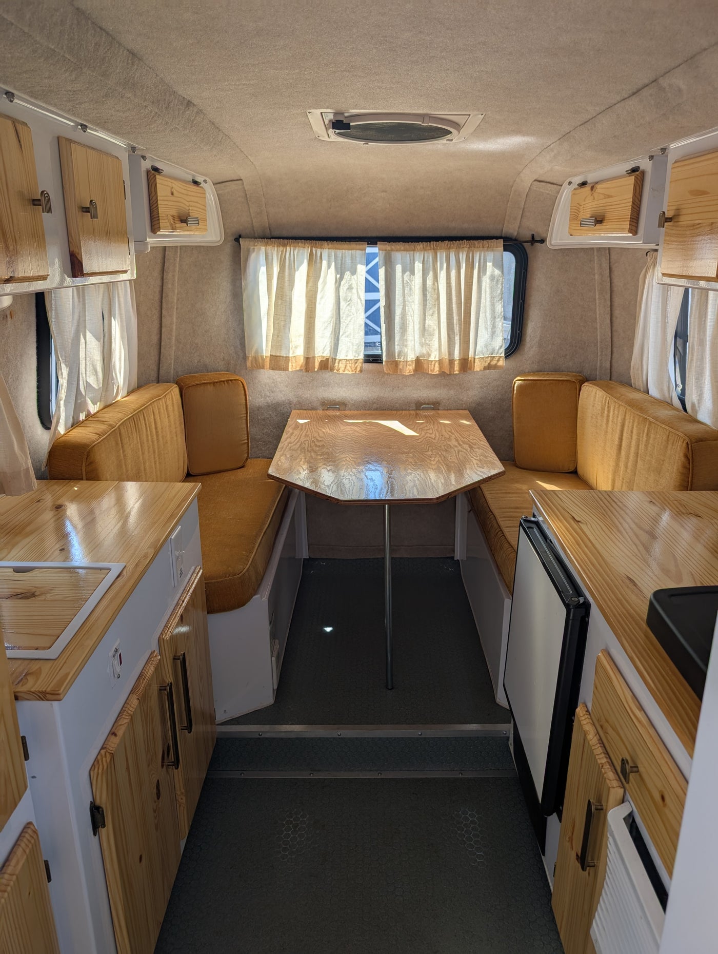 View inside a bright rv rental. Features a central wood dinette, golden cushioned benches, — photo 6