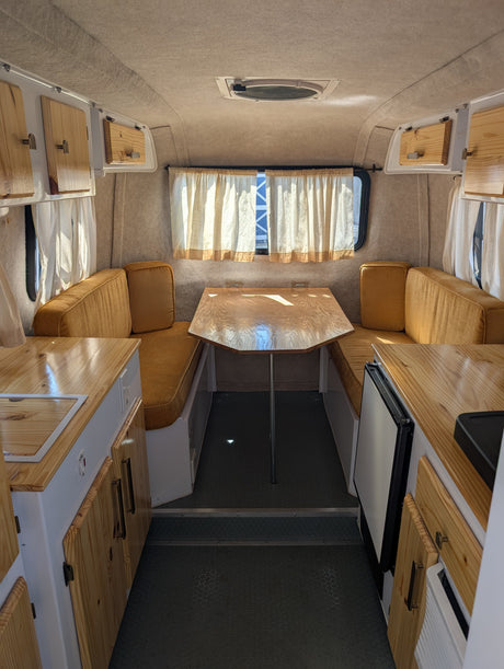 View inside a bright rv rental. Features a central wood dinette, golden cushioned benches,