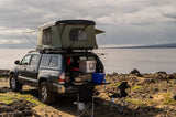 Overland RV rental: A dark pickup truck with a rooftop tent and tailgate camp kitchen by a vast body of water.