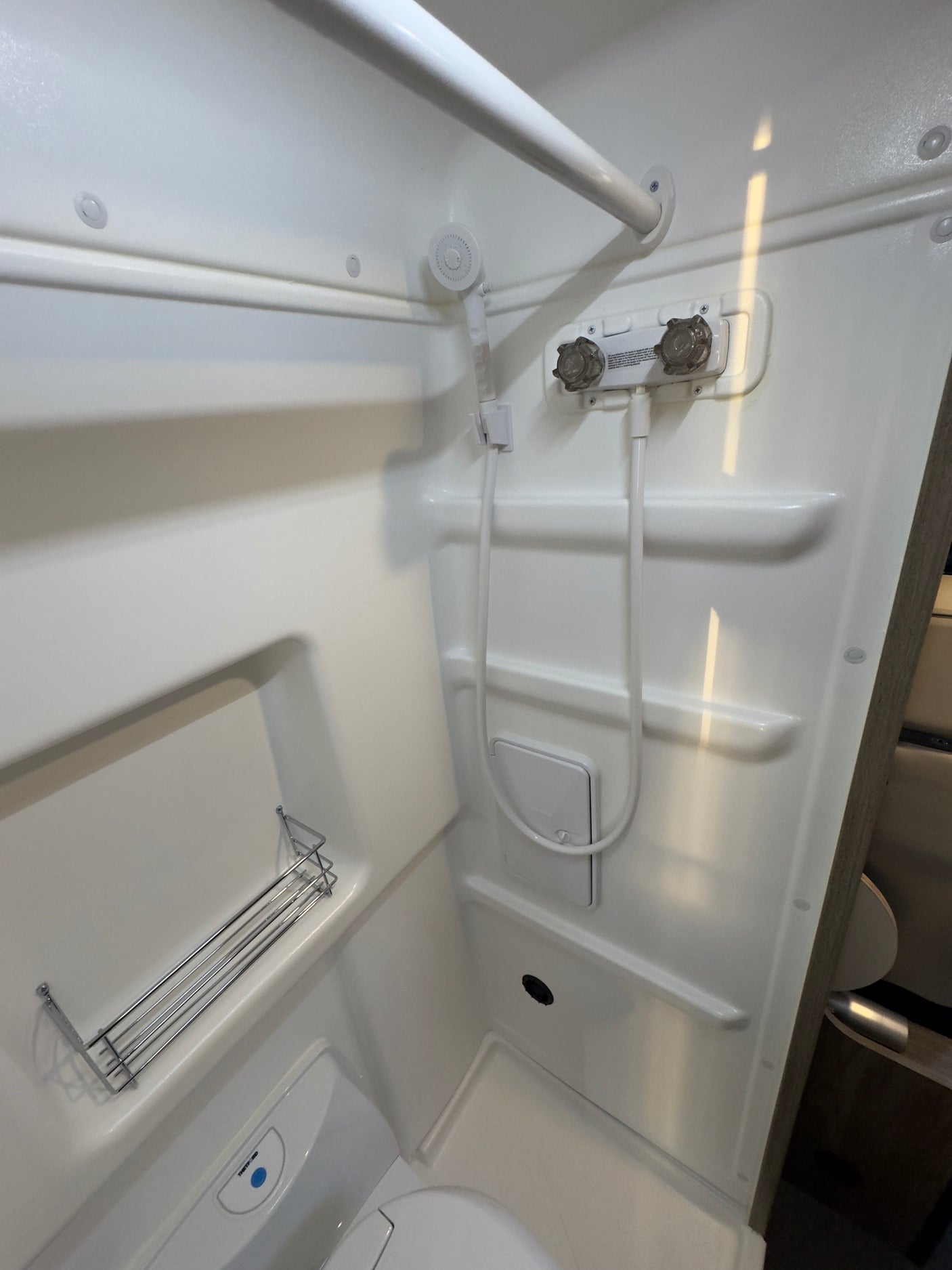 Compact RV rental bathroom, featuring a white shower, handheld showerhead, toilet, and storage shelves.