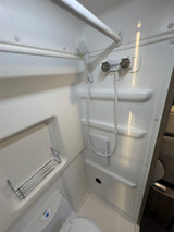 Compact RV rental bathroom, featuring a white shower, handheld showerhead, toilet, and storage shelves.