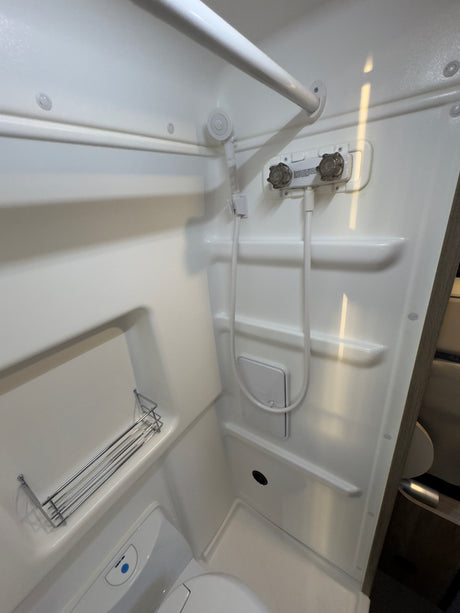 Compact RV rental bathroom, featuring a white shower, handheld showerhead, toilet, and storage shelves.