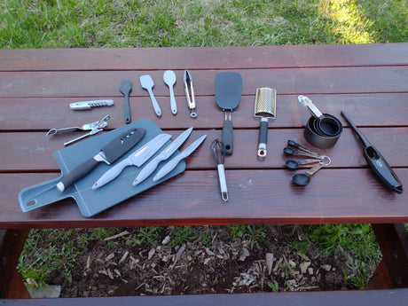 RV rental kitchen essentials: knives, spatulas, measuring tools, and more neatly arranged on an outdoor picnic table.