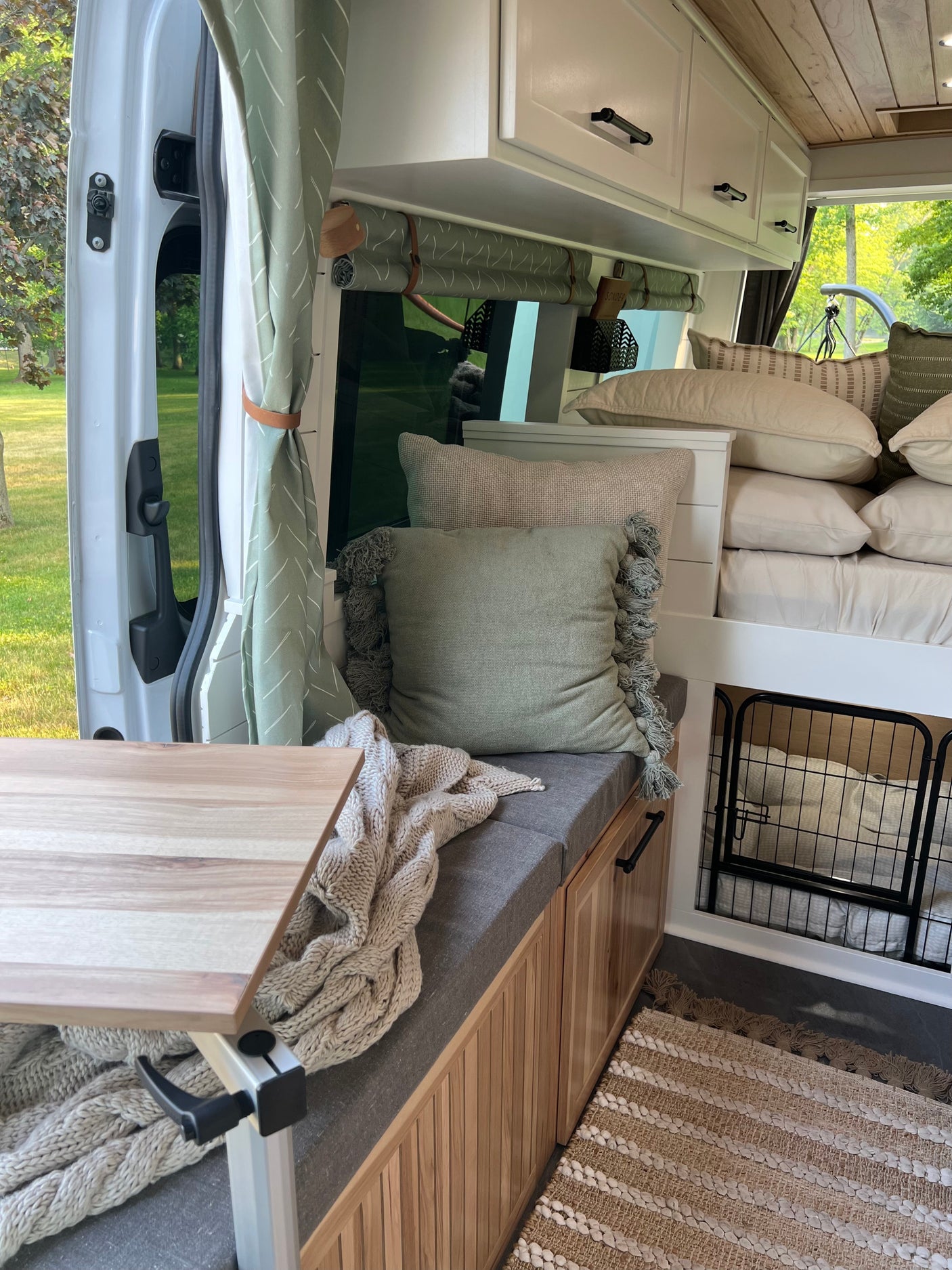 Inviting rv rental interior features a cozy bed, dining area, dog crate, and sage green decor with wood accents.