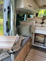 Inviting rv rental interior features a cozy bed, dining area, dog crate, and sage green decor with wood accents.