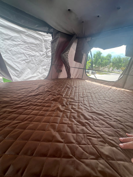 Cozy RV rental interior: a comfortable brown quilted mattress with a view of the outside. Ideal for camping.