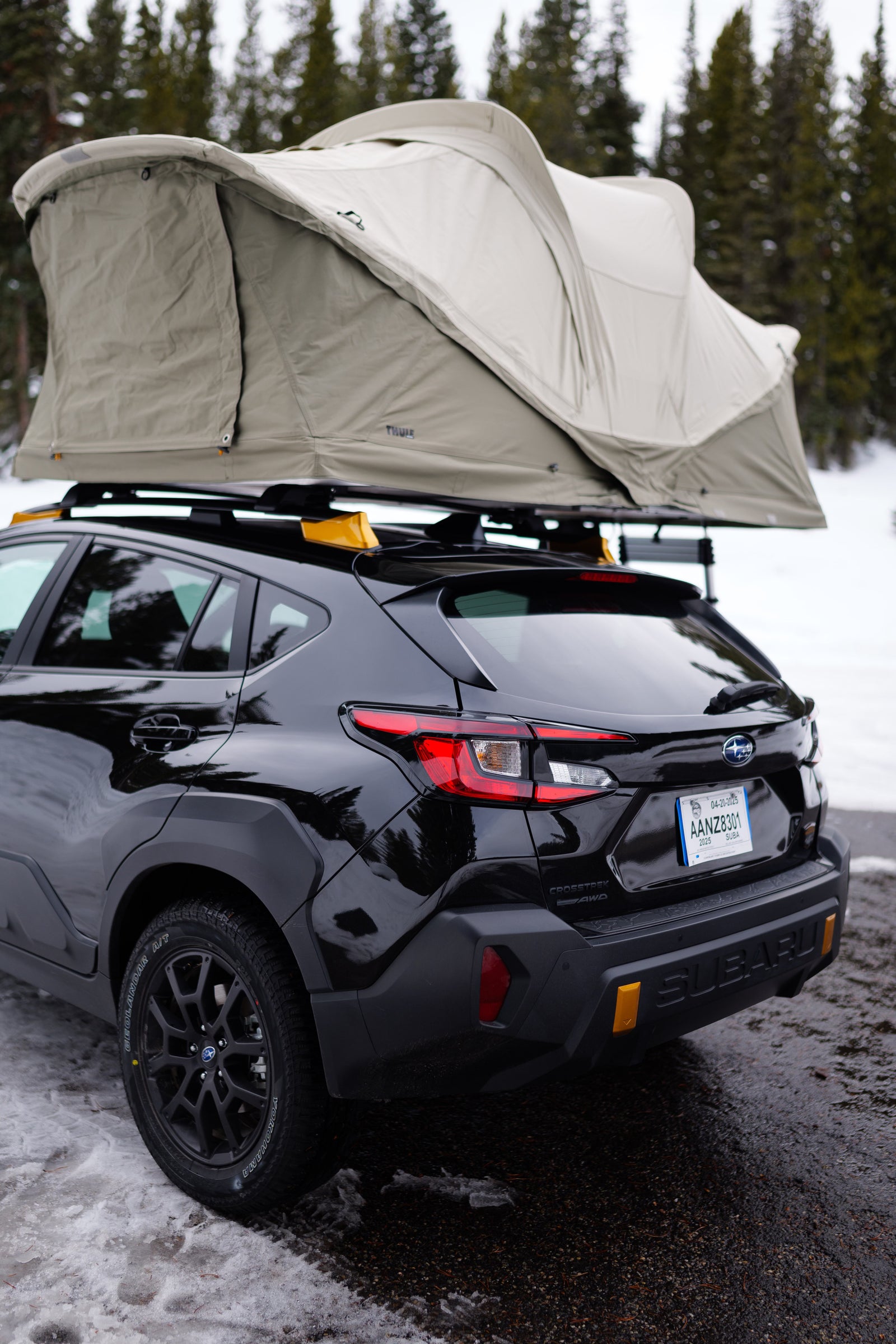 Black Subaru Crosstrek with a Thule rooftop tent, parked in a snowy forest, an agile option for an RV rental adventure.