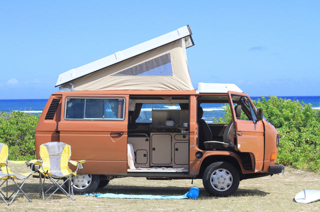 This brown VW camper van with pop-top roof and open interior offers an ideal rv rental for beach camping.