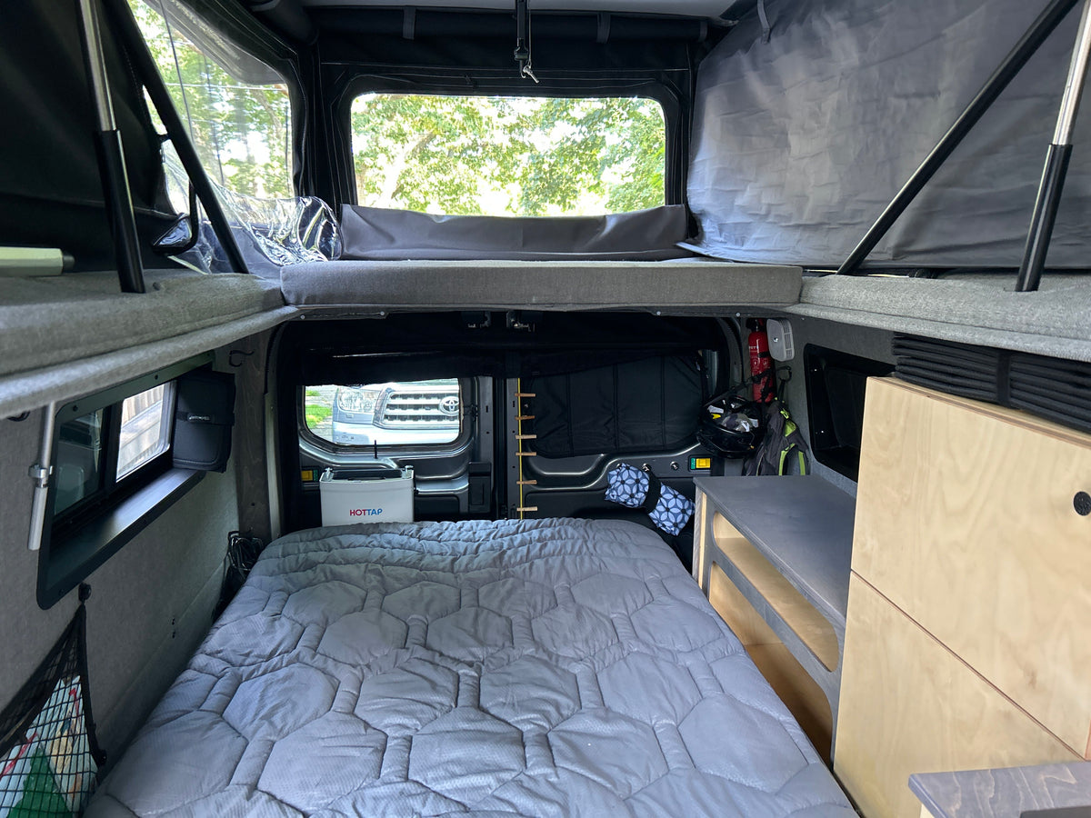 Inside a cozy RV rental camper van, featuring a main bed, a pop-top bed, and organized storage. — photo 4