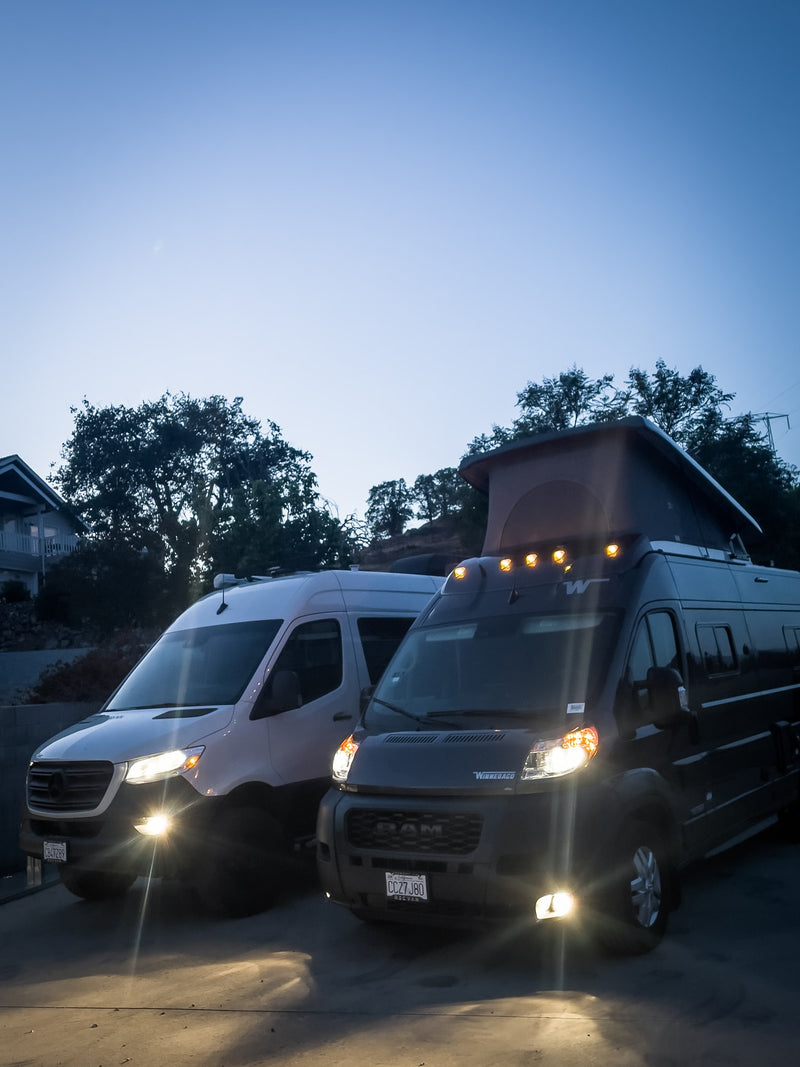 Two modern rv rental camper vans, a white Mercedes Sprinter and a dark Winnebago with a pop-top, are parked at dusk. — photo 20