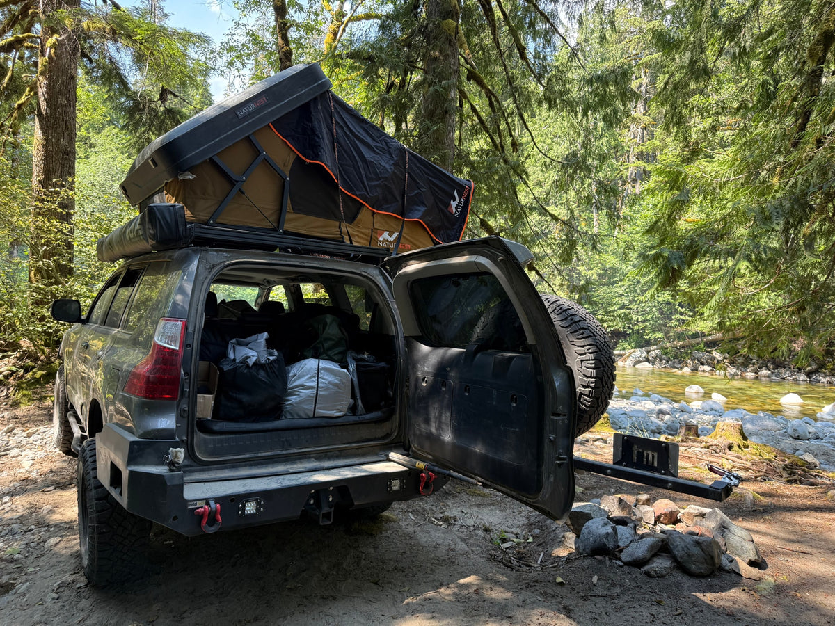  parked in a forest by a rocky river.|Adventure-ready SUV with rooftop tent & gear parked by a clear forest river — photo 8