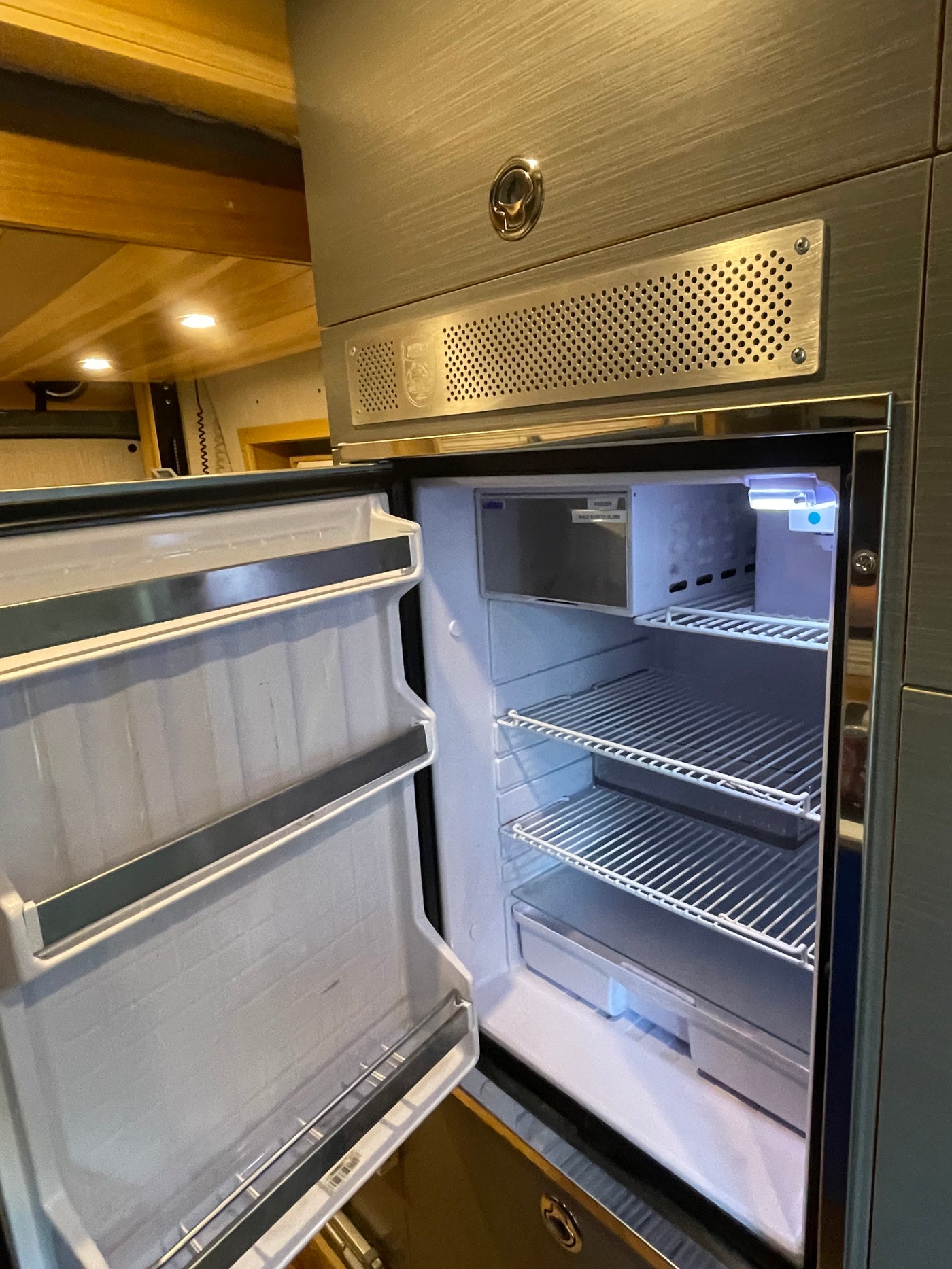Inside a spotless rv rental fridge, showcasing its open door, wire shelves, small freezer, and interior light for travelers. — photo 17