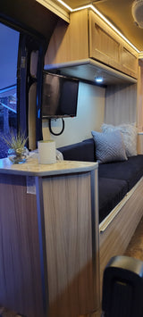 Explore this RV rental's cozy living space, featuring a TV, dark sofa with pillows, and warm ambient lighting.