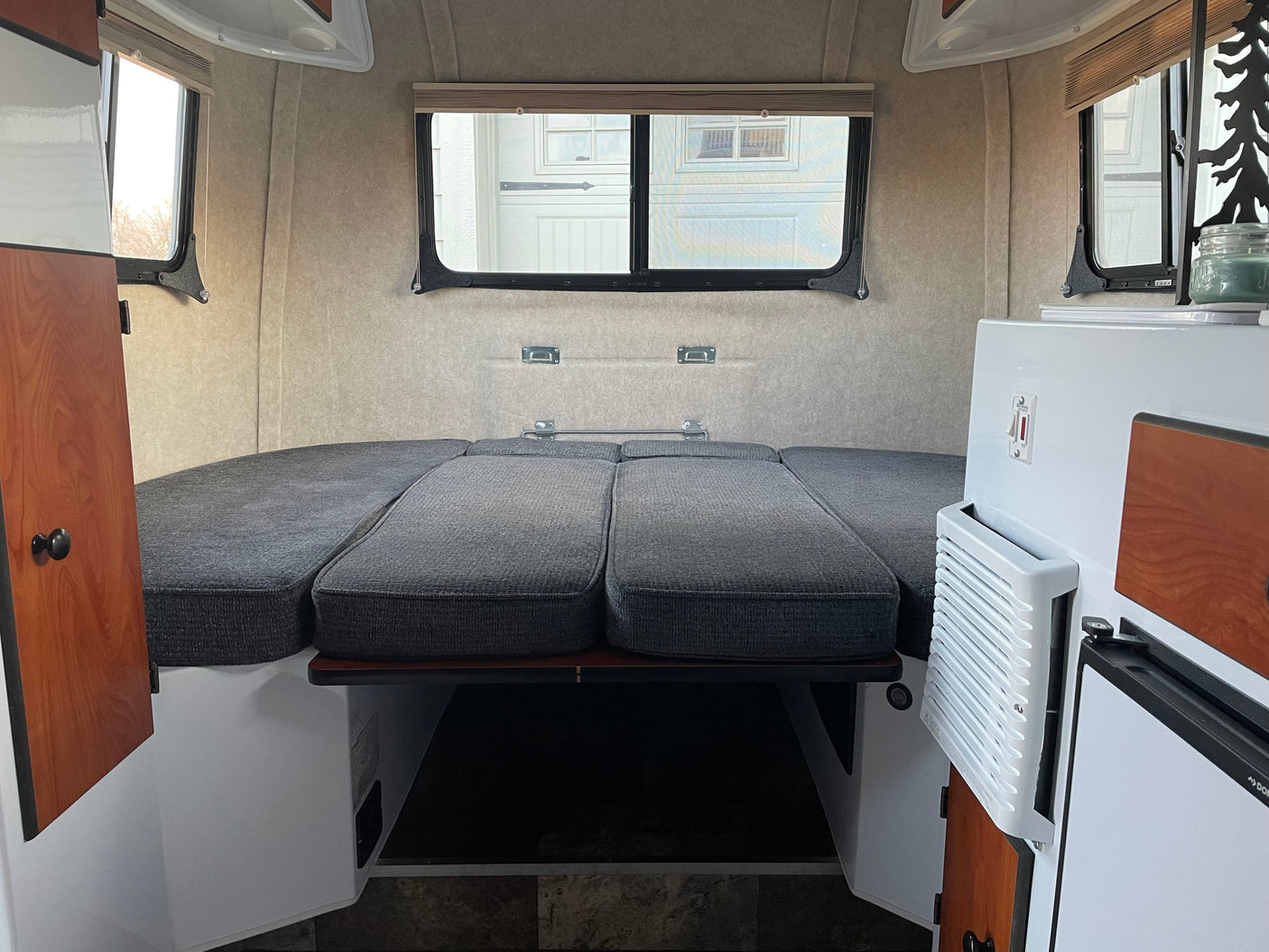 Inside a cozy rv rental, showcasing a comfortable bed, large windows, and built-in amenities like a fridge.