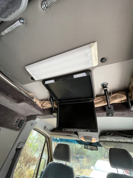 RV rental interior with a flip-down monitor, bright ceiling light, and upholstered overhead storage for comfort.