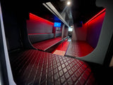 Inside this premium rv rental: A dark, modern interior with long, diamond-quilted benches, vibrant red LED strip lights, and entertainment screens.
