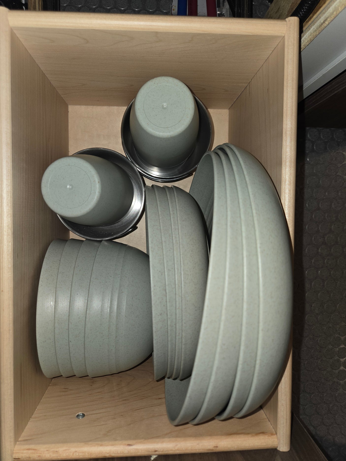 RV rental kitchen: Lightweight, stackable bowls and cups (some in metal holders) neatly organized in a wooden drawer.