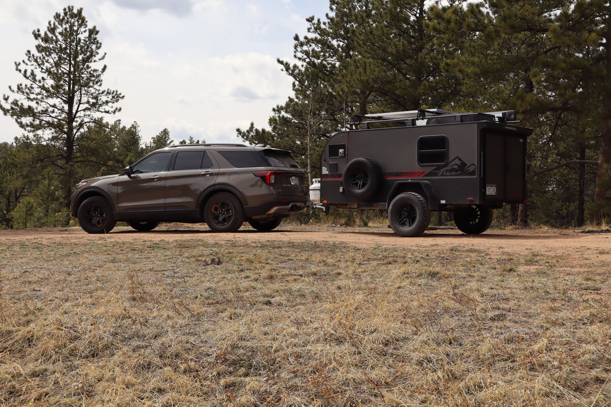 Adventure awaits! This SUV tows a rugged RV rental through a forest, ready for off-road camping.